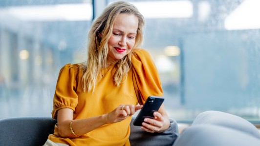 Kvinne leser på mobilen i sofa