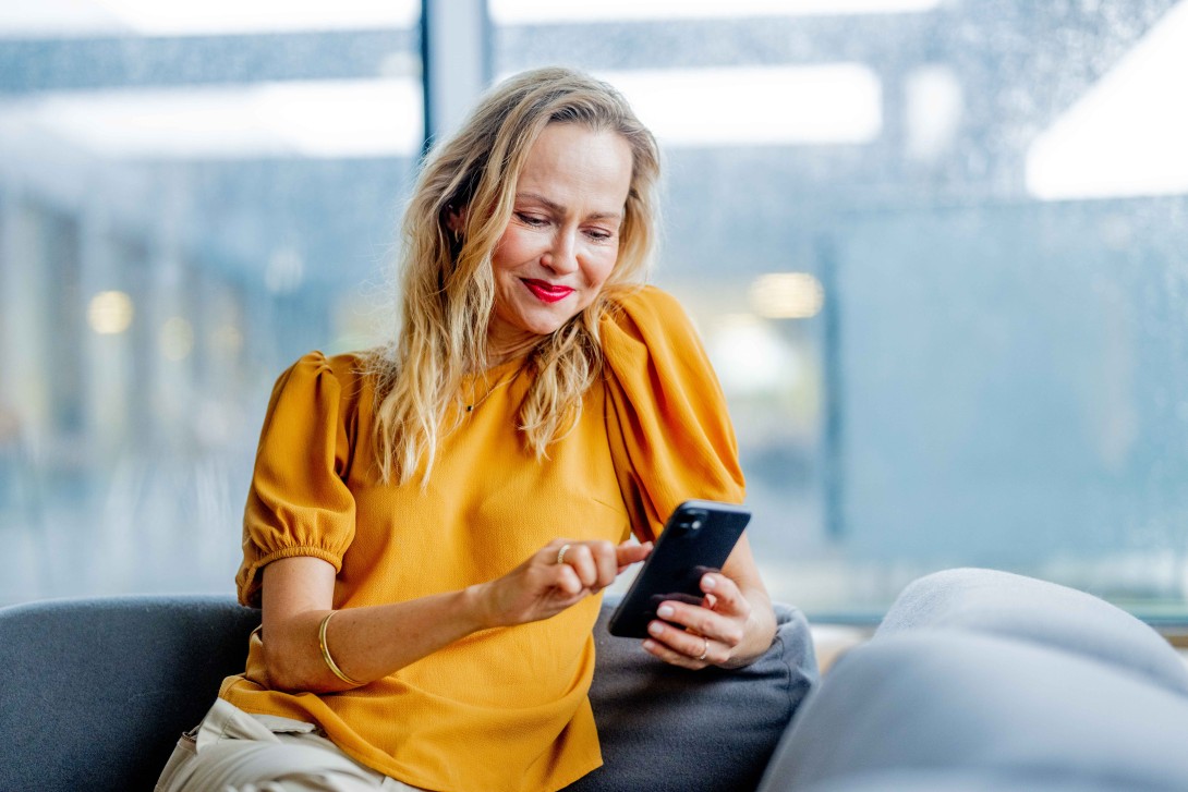 Kvinne leser på mobilen i sofa